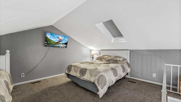Cama queen en el dormitorio del loft. El loft tiene un televisor Roku.