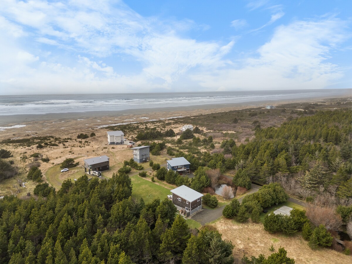 An aerial view captures a serene landscape featuring a row of modern homes nestled among lush greenery, with a beach and ocean visible in the background. The expansive grounds provide open space and a sense of privacy, enhancing the coastal setting.