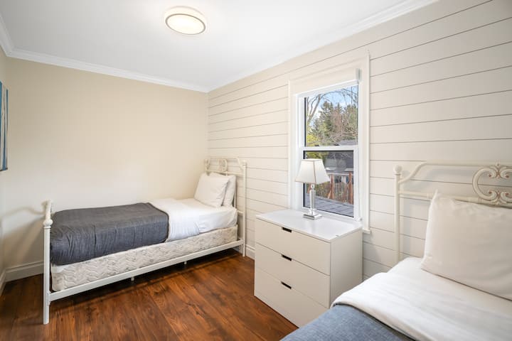 Guest bedroom with two single beds, clean linens, dresser, roller shades.