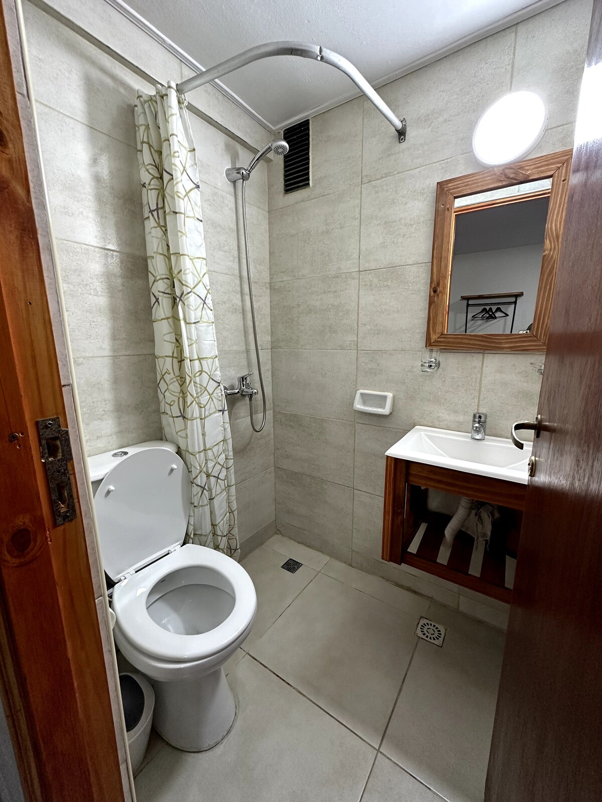 An efficiently designed bathroom is featured, showcasing modern fixtures. A shower with a glass door is included, accompanied by a sink with storage underneath. A small mirror hangs above the sink, and a light source is positioned above the mirror, enhancing visibility.