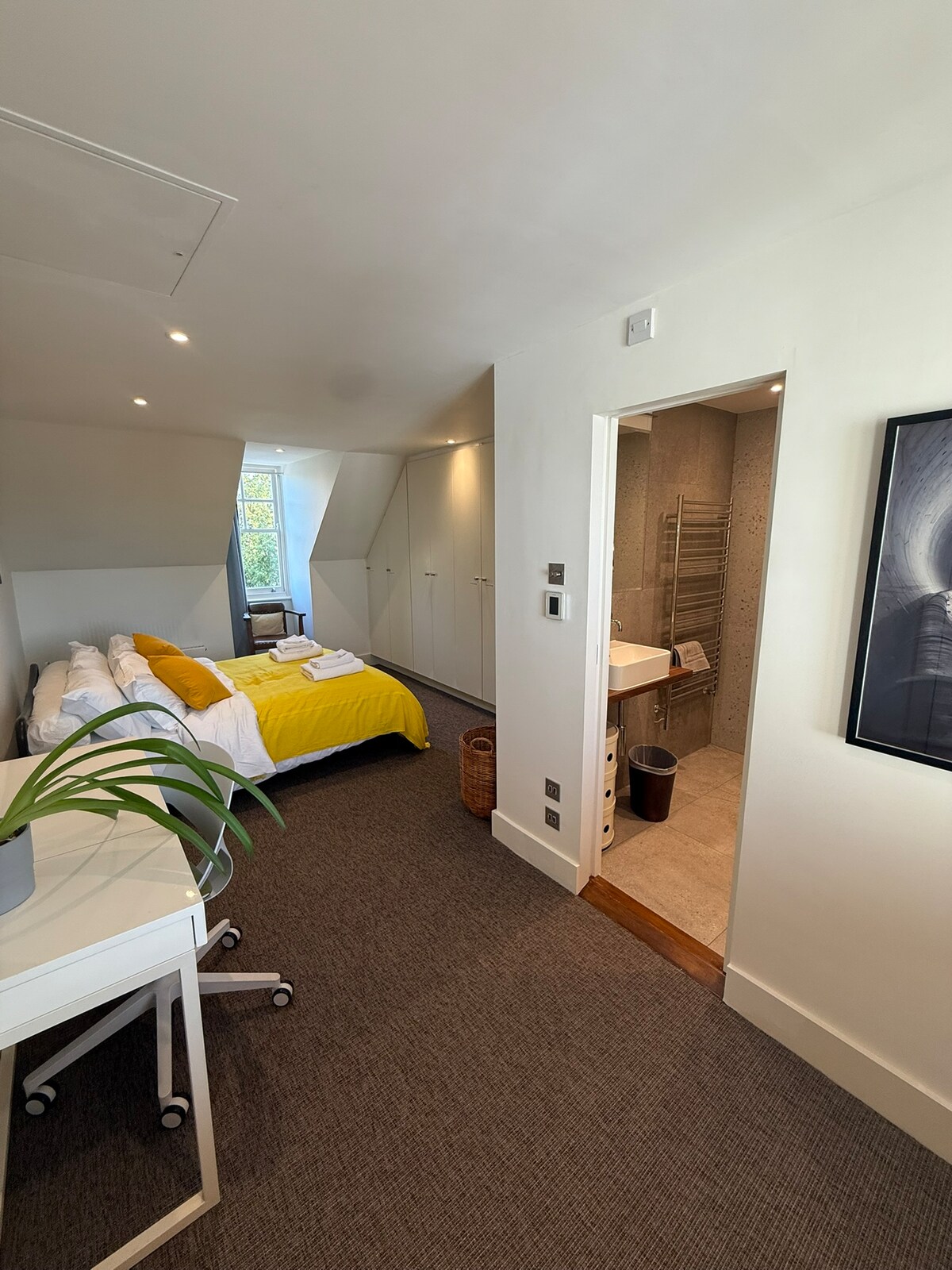 ห้องนอนใหญ่มีเตียงคิงไซส์ โต๊ะทำงานแบบบาง และห้องน้ำในตัวใหม่ที่มีกระเบื้องเทอร์ราซโซ