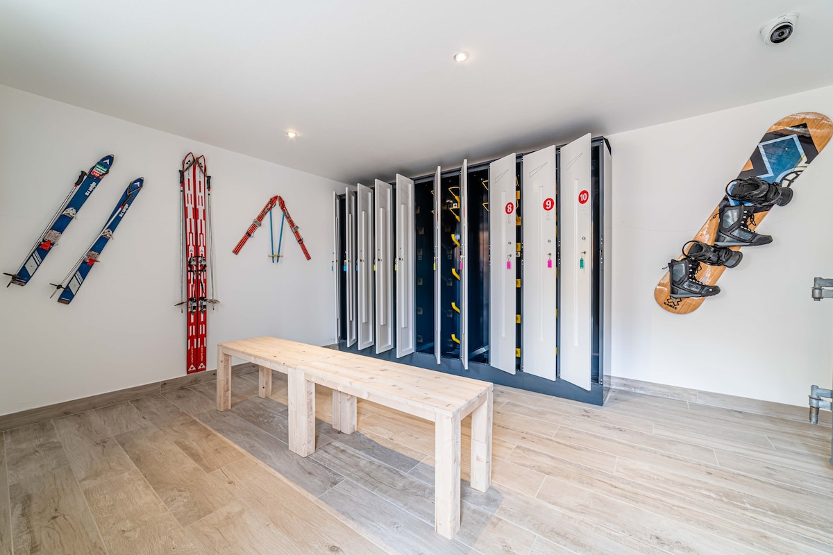 A dedicated ski storage area is visible, featuring wooden benches and multiple lockable storage units. Ski equipment is displayed, including colorful skis and a snowboard mounted on the wall. The floor exhibits a tiled wood effect, contributing to the functional space.