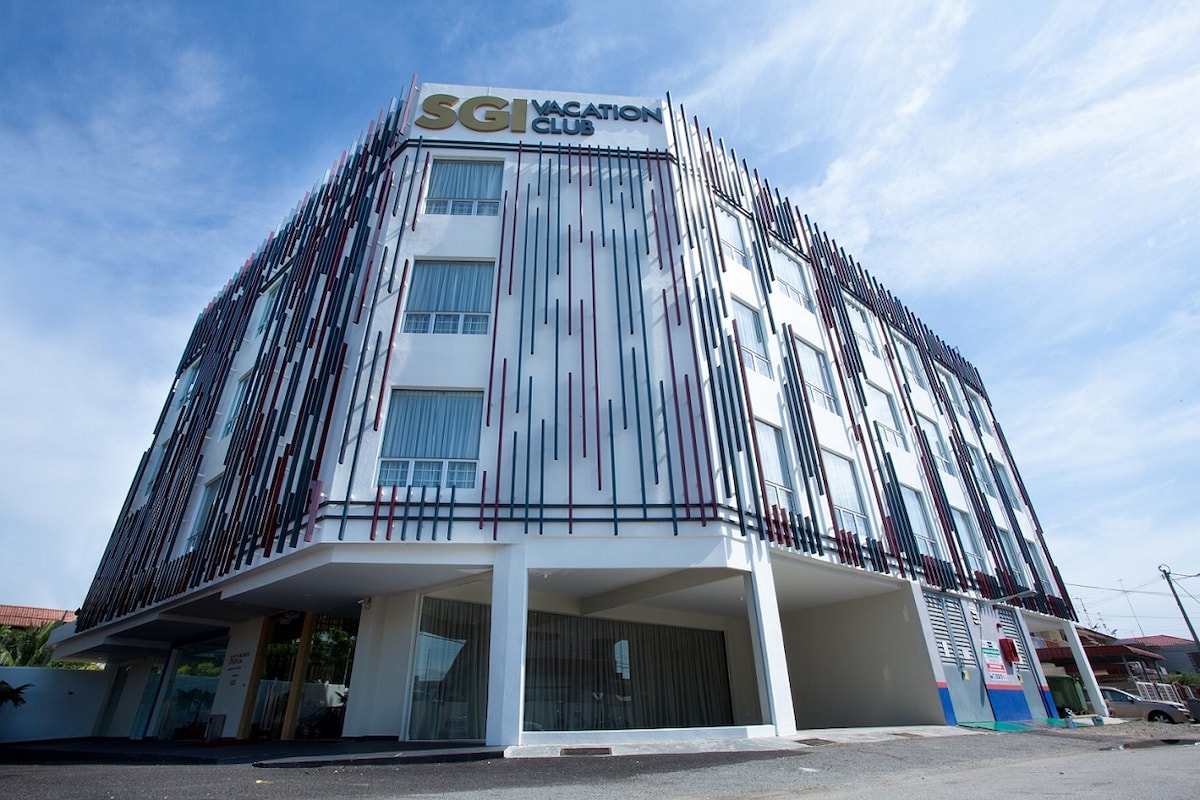 The exterior of SGI Vacation Club Hotel Melaka features a modern design with a striking facade characterized by vertical accents. The three-story building is complemented by large windows, allowing natural light to fill the interior spaces. A clear blue sky serves as a backdrop.