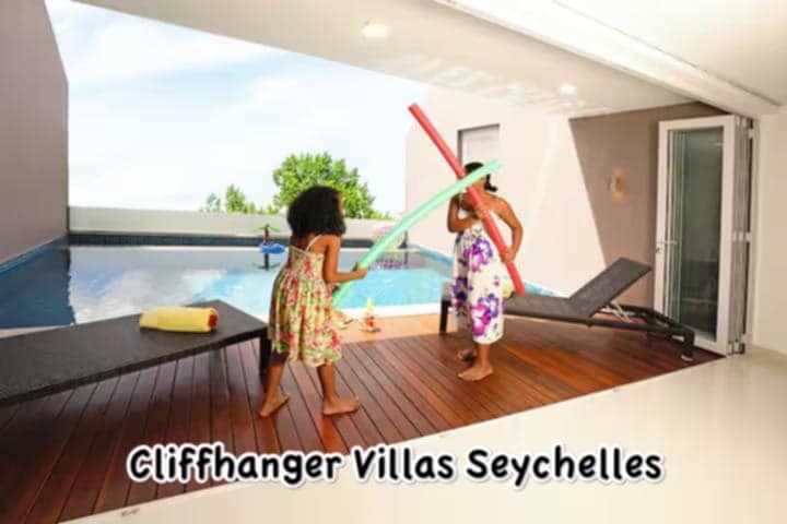 A spacious terrace features a private swimming pool, flanked by lounge chairs. Two children engage in playful activity with colorful foam noodles. Lush greenery is visible in the background, providing a serene view from the villa.