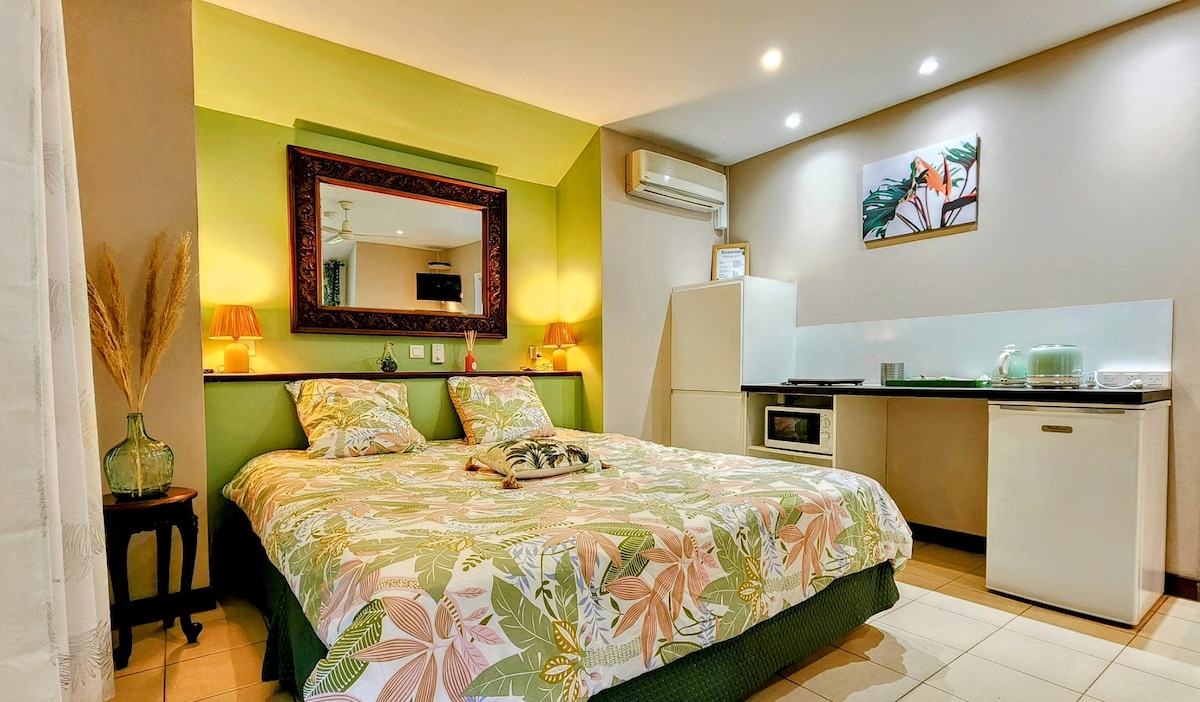 A spacious sleeping area is furnished with a large floral-patterned bed and matching bedside lamps. A mirror reflects soft lighting, and a kitchenette is located in the corner, featuring a refrigerator and a microwave, providing essential cooking amenities.