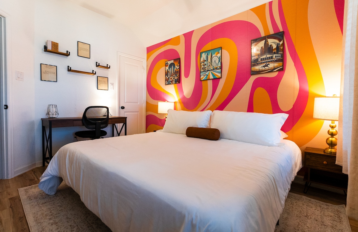 Relax in this spacious king bedroom featuring bold retro decor, a cozy work desk, and warm lighting. The groovy accent wall adds a playful touch, making this space both stylish and comfortable for work or rest.