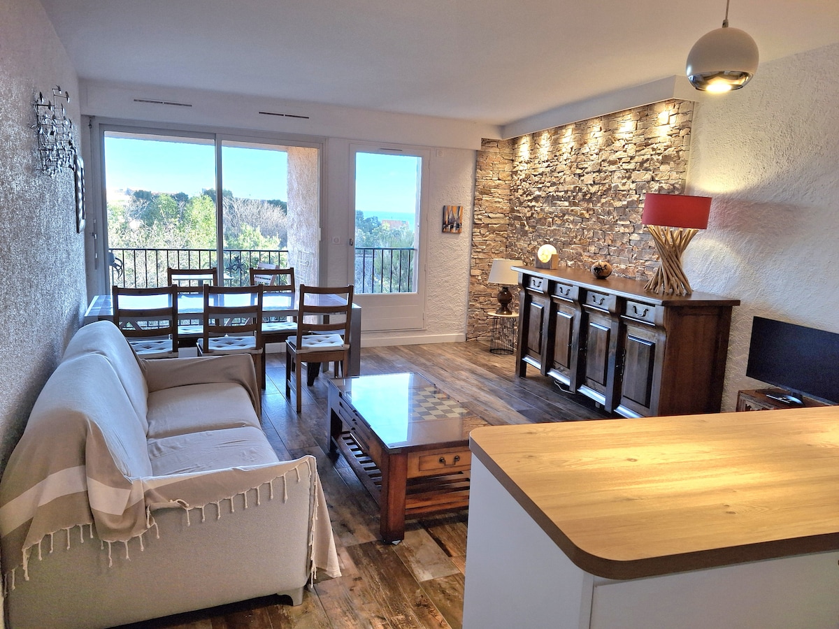 A bright living area features a cozy sofa and a wooden coffee table. Large glass doors open to a balcony, providing access to natural light and outdoor views. Tasteful stone accent walls add character, while wooden furniture offers a warm ambiance.