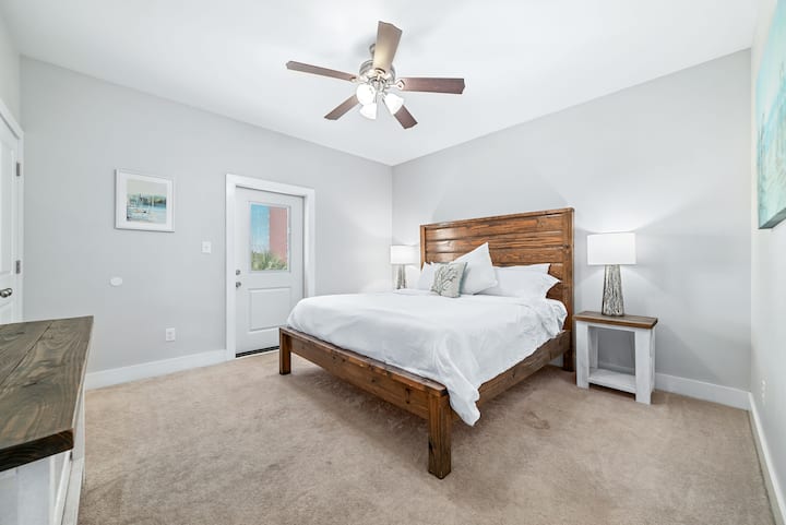 Во оваа шармантна спална соба е прикажана дрвена рамка за кревет со свежа бела постелнина, ламба инспирирана од крајбрежјето и едноставни уметнички дела. Кадифените теписи и пристапот до приватниот поплочен двор го подобруваат просторот, што го прави мирно прибежиште за мирни ноќи покрај море!