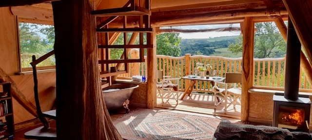 An inviting interior features a spiral staircase leading to a mezzanine level. A cozy living space includes a wood-burning stove, a copper bathtub, and a small table set with two chairs, offering scenic hillside views through large windows.