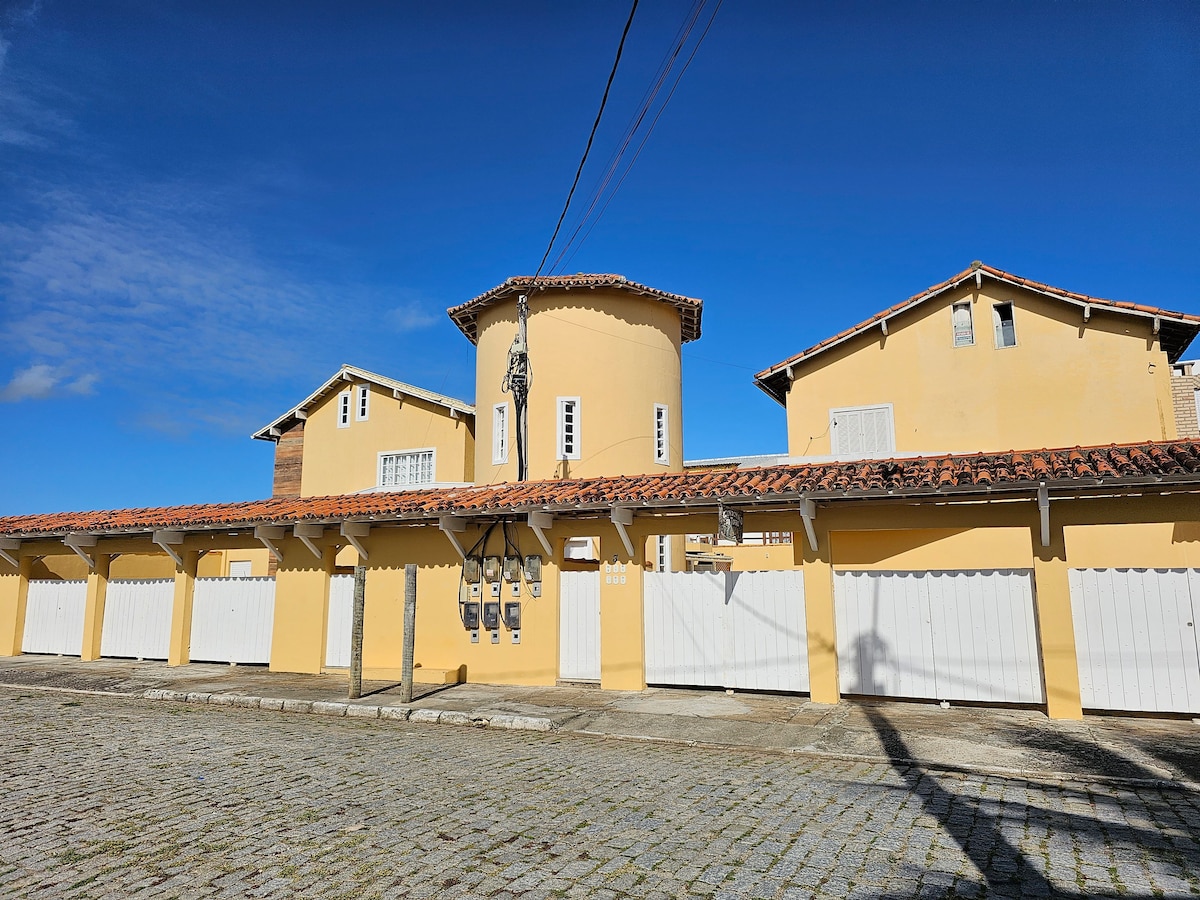 A two-story yellow building features a round tower at the center, creating a unique architectural focal point. The structure includes several garage doors at the base, with a clear blue sky overhead, enhancing the overall bright appearance.