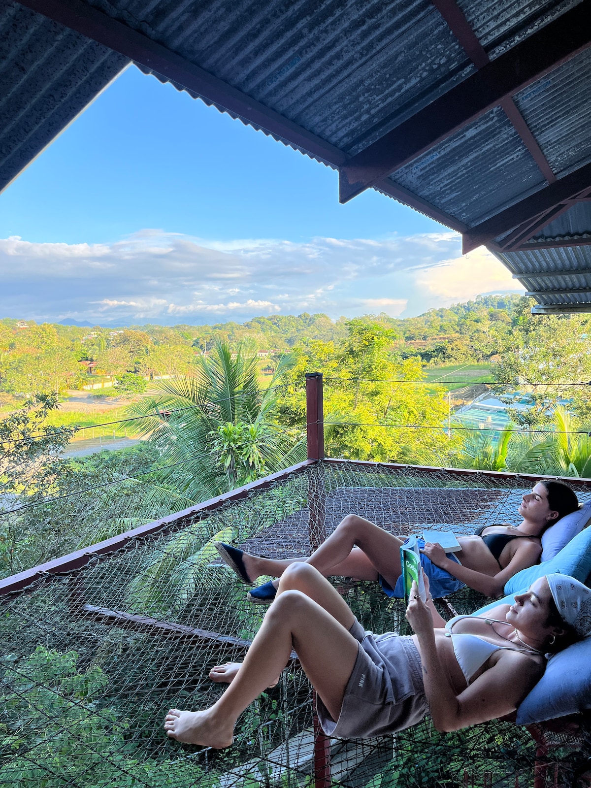 An elevated hammock offers a serene spot for relaxation, surrounded by lush greenery and sweeping views of the landscape. The gentle sway invites guests to unwind, while the clear blue sky enhances the tranquil atmosphere.