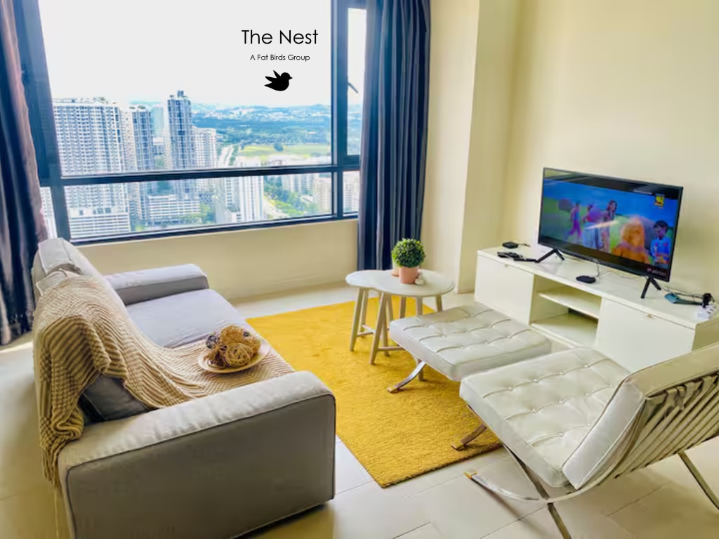 A bright living area is showcased with a large window revealing a cityscape view. A sofa, draped with a soft throw, faces a coffee table. A TV set is positioned opposite, accompanied by two modern chairs. A potted plant adds a touch of greenery.