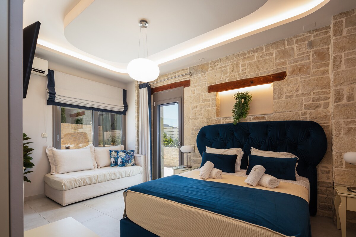 King-size ensuite bedrooms (1.60 x 2.00) and a two-seater sofa bed that can accommodate one guest if needed. A 32” Smart TV is wall-mounted, and patio doors lead to the shared veranda. 
