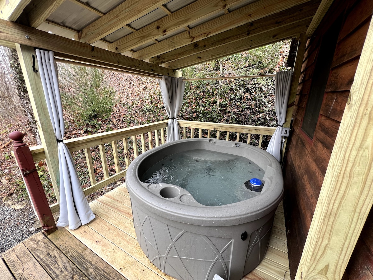 A hot tub is situated on a wooden deck, surrounded by protective curtains. The structure offers privacy while allowing views of the natural surroundings. Water can be seen gently rippling, inviting relaxation and tranquility.