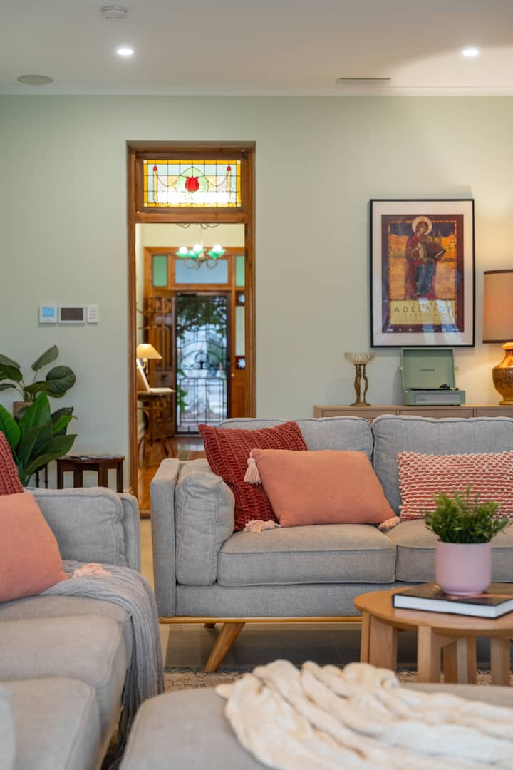 Pumzika katika sebule ya nyumbani iliyo na sofa za kijivu, vivutio vyenye joto na mwonekano wa kupendeza wa mlango wa kioo wenye madoa. Inafaa kwa ajili ya kupumzika kwa mtindo na starehe.