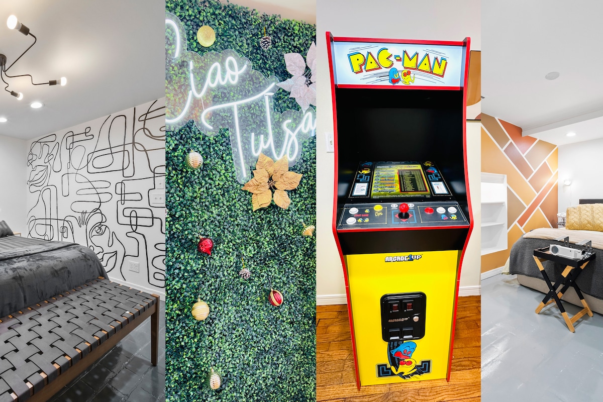 A vibrant hand-painted accent wall complements a cozy sleeping area with a decorative bed frame. Greenery adorned with decorative elements adds a refreshing touch, while a decorative light fixture hangs above. A classic arcade Pac-Man machine is set against a colorful backdrop, enhancing the entertainment offerings.