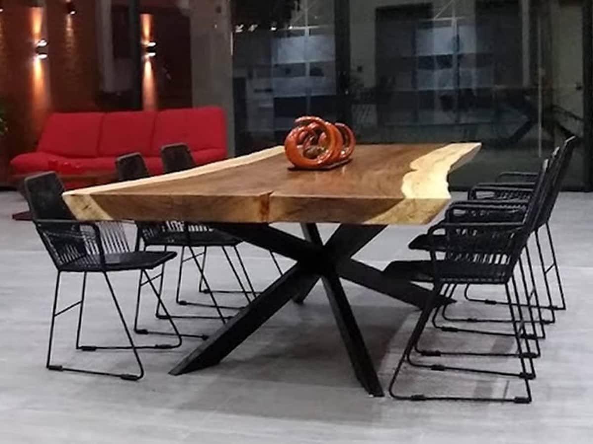 A large wooden dining table with a natural edge is positioned centrally, supported by a striking black base. Six black wire chairs surround the table, enhancing the modern feel of the space, with ambient lighting softly illuminating the area.