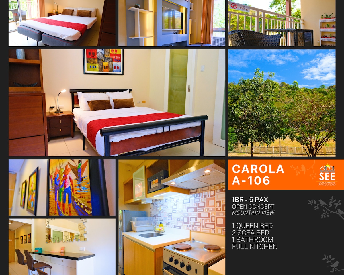 An open-concept layout is presented, featuring a queen bed with vibrant accents. Two sofa beds are arranged nearby. A kitchen with modern appliances is visible, and artwork adorns the walls. Large windows provide a view of lush greenery outside, enhancing the connection to nature.