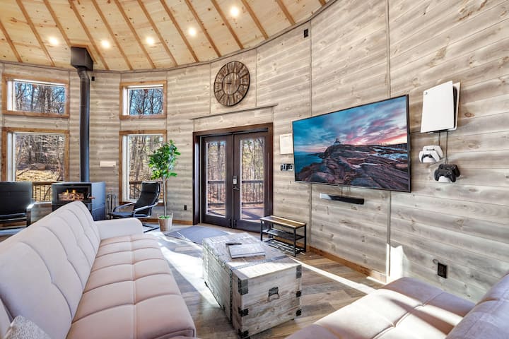 Main living area with a large wall-mounted TV and PlayStation 5, a comfortable sectional, and the wood stove close by.