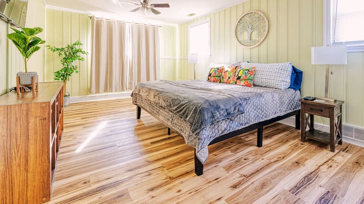 A cozy, well-lit bedroom featuring a comfortable bed with vibrant pillows, wooden furniture, and light-colored walls, creating a peaceful and inviting atmosphere.