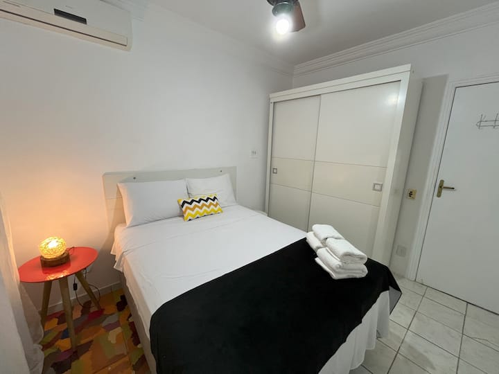 غرفة نوم مع مكيف هواء ومروحة سقف وتعتيم وخزانة ملابس ومرآة وبياضات أسرّة ومناشف.