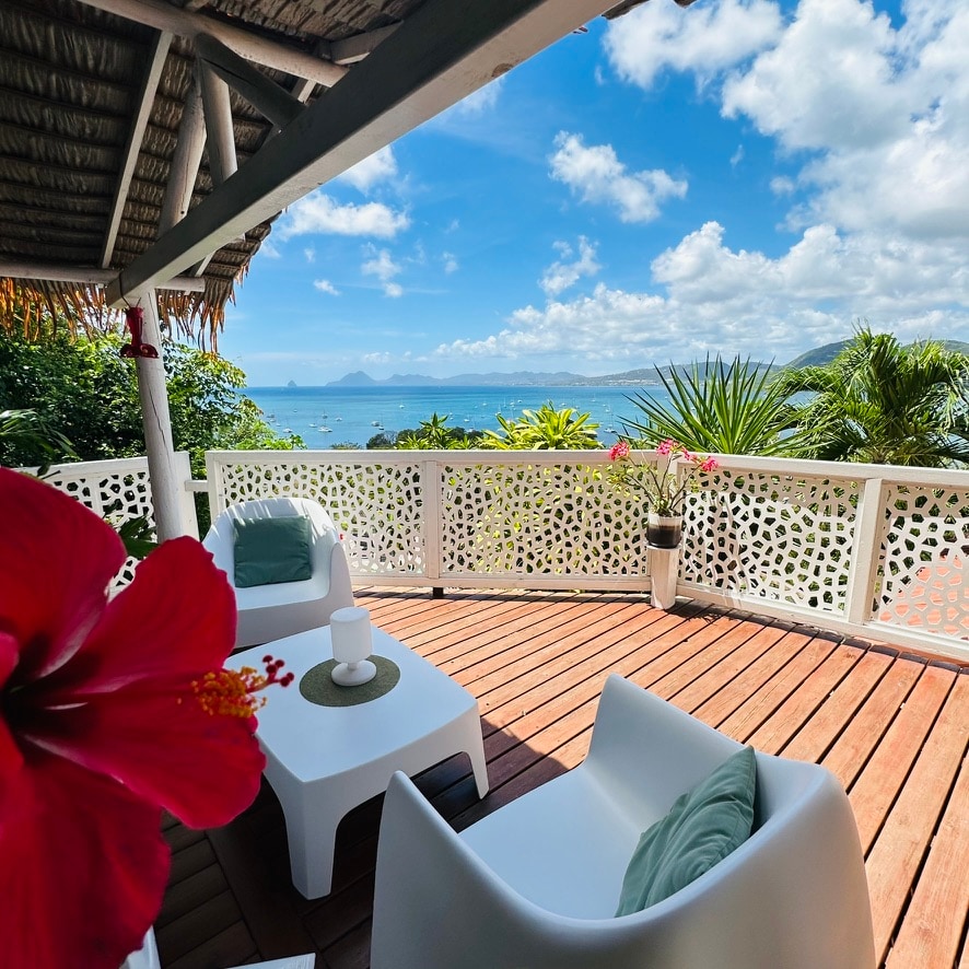 A spacious terrace is presented, featuring comfortable outdoor seating positioned to enjoy the panoramic view of the Caribbean Sea. Lush greenery and a vibrant flower add natural splashes of color, while the sea breeze invites relaxation in this tranquil setting.