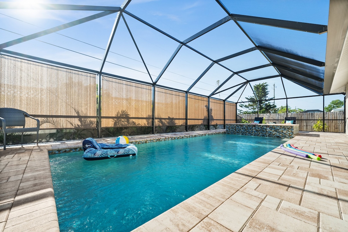 A spacious outdoor area features a heated saltwater pool, surrounded by a newly constructed screened enclosure. Relaxing seating is available nearby, with colorful pool floats resting on the water's surface. Sunlight filters through the mesh, creating a tranquil atmosphere.