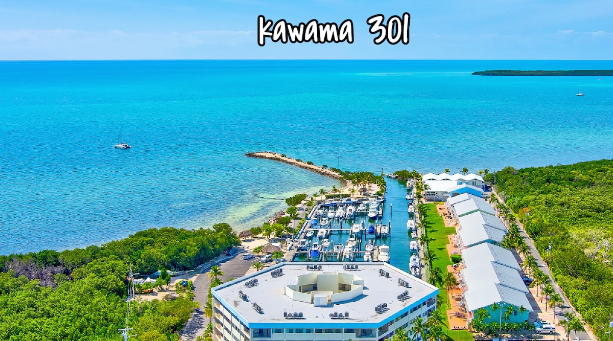 An aerial view captures the Kawama Yacht Club, featuring a marina filled with boats alongside lush mangroves and vibrant turquoise waters. The surrounding landscape reflects the tranquility and scenic beauty of the oceanfront location, showcasing an inviting setting for relaxation and recreation.