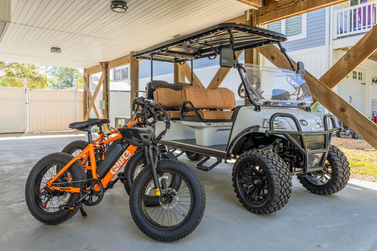 An electric golf cart and two bicycles are parked under a covered area. The golf cart features cushioned seating and sleek design, while the bicycles have large tires, suitable for various terrains. The concrete floor is clean and well-maintained, providing ample space.