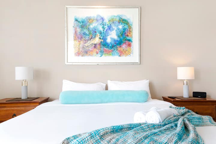 Zen Paradise Seaside Serenity Experience ელეგანტურობა და სიმეტრია ჩვენს ოთახში, სადაც ლუქს-კლასის საწოლი დგას ორი ელეგანტური გვერდითი მაგიდით, მიმზიდველი ნახატით, რომელიც ამშვენებს სივრცეს და ქმნის ჰარმონიულ დასვენებას