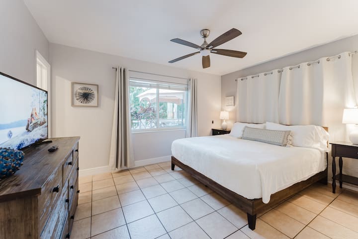Master bedroom with king bed dressed in hotel-quality linens, ceiling fan, and smart TV. A large window brings natural light and direct access to outdoor views, while ample storage and a private en-suite bathroom make it ideal for extended stays.
