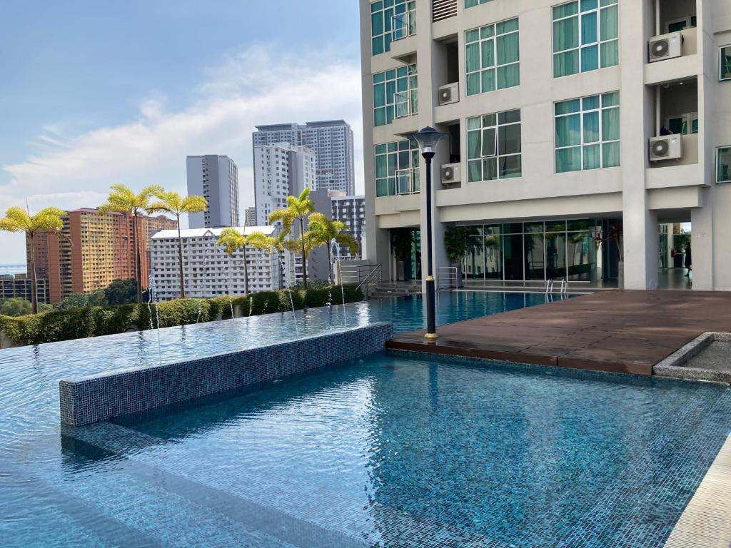 An outdoor infinity pool is visible, surrounded by greenery and modern buildings. Sunlight reflects off the water's surface, creating a tranquil setting. Tall palm trees line the edge, and lounge areas are positioned nearby, enhancing the inviting ambiance of the space.