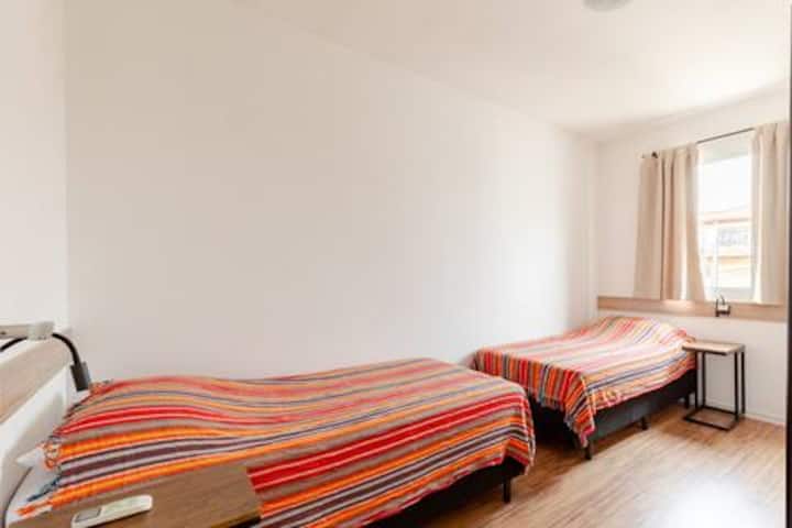 Cuarto 1 con baño privado, tres camas individuales, aire acondicionado, cortina opaca, mantas, almohadas y ropa de cama adicionales.