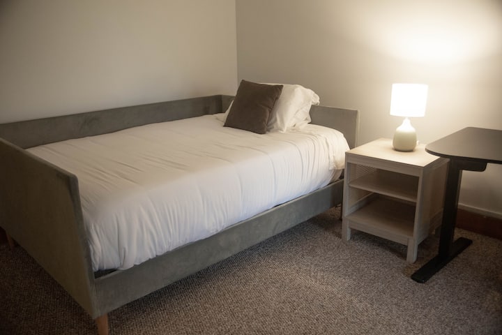 تحتوي الغرفة متعددة الأغراض في الطابق السفلي على سرير نهاري عصري مع فراش فخم ومصباح سرير متوهج وطاولة عمل صغيرة - مثالية للاسترخاء أو متابعة القليل من العمل أثناء إقامتك.