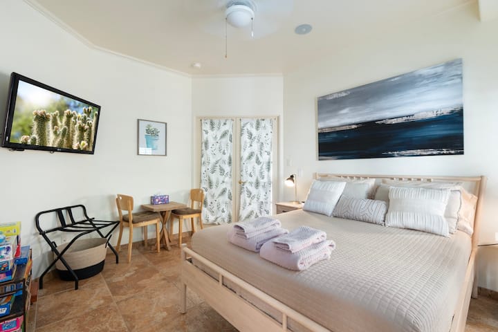 Inviting queen bedroom just off the main living space, featuring soft natural light, cozy décor, and a comfortable seating area. Includes a mounted TV, small table, and ample space to relax, creating a peaceful retreat for your Sedona stay.