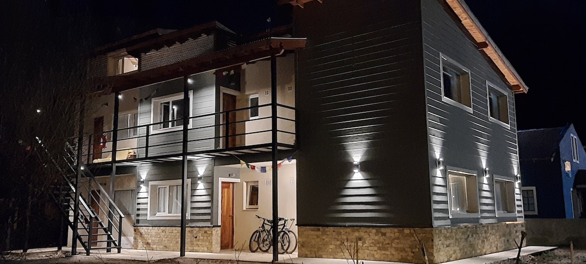 The exterior of the building is illuminated at night, showcasing a two-story structure with a spacious porch and large windows. An outdoor staircase leads to the second floor, while bicycles are parked nearby, inviting outdoor exploration.