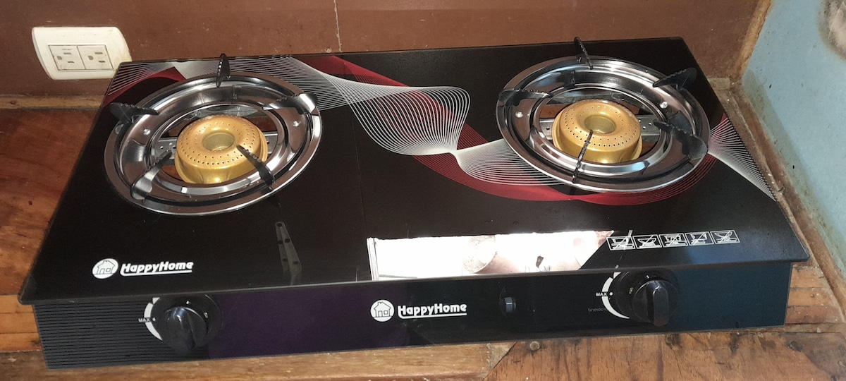 A two-burner gas stove with a sleek black surface is displayed on a wooden countertop. Each burner is equipped with a golden flame ring, designed for efficient cooking. The stove features clearly labeled knobs for easy operation.