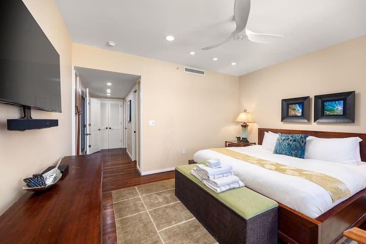 Hauptschlafzimmer mit einem Kingsize-Bett, einer gemütlichen Bank und einem Flachbildfernseher. Holzakzente und warmes Licht unterstreichen die einladende Atmosphäre und bieten einen ruhigen und stilvollen Raum, um sich nach einem langen Tag zu entspannen.