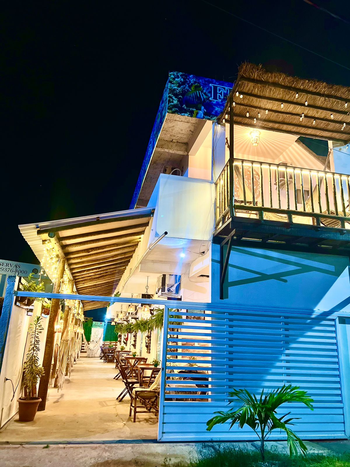 A multi-level building is illuminated at night, showcasing a welcoming entrance. The exterior features a combination of wood and modern materials, with outdoor seating available along the pathway. Soft lighting enhances the ambiance, creating a serene atmosphere suitable for evening relaxation.