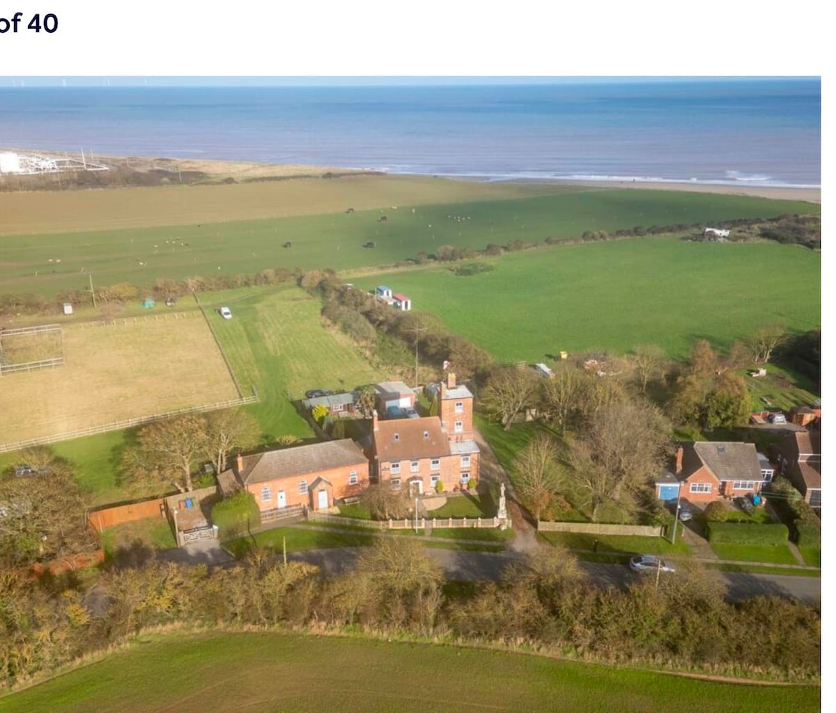 An aerial view captures the charming former Methodist Chapel surrounded by lush green fields and patches of cultivated land. The coastline is visible in the distance, illustrating the property's proximity to the beach, while the peaceful rural landscape enhances the tranquil setting.