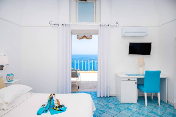 غرفة نموذجية على طراز بوسيتانو مع بلاط مرسوم يدويًا وشرفة واسعة تطل على البحر وحمام فاخر."