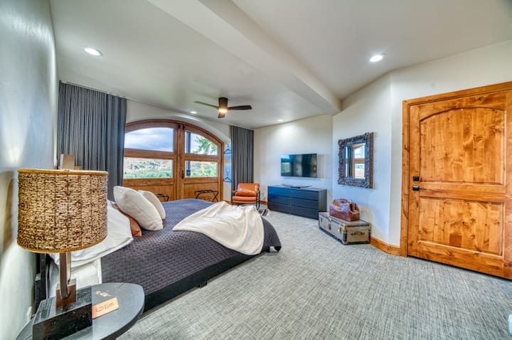 غرفة نوم فاخرة في بوزمان مع أبواب خشبية مقوسة وفراش فاخر وديكور دافئ. استمتع بالضوء الطبيعي والأثاث الحديث واللمسات المريحة، المثالية للاسترخاء بعد استكشاف المناظر الطبيعية الشتوية في مونتانا أو الاستمتاع بملاذ هادئ في الداخل.