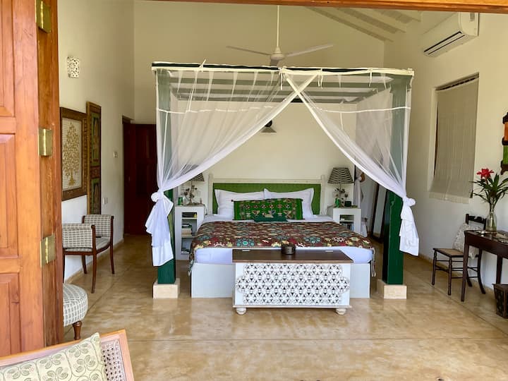 Dormitorio principal con cama tamaño king y baño privado. Las persianas de madera se abren a la terraza y a la vista del campo de arroz.