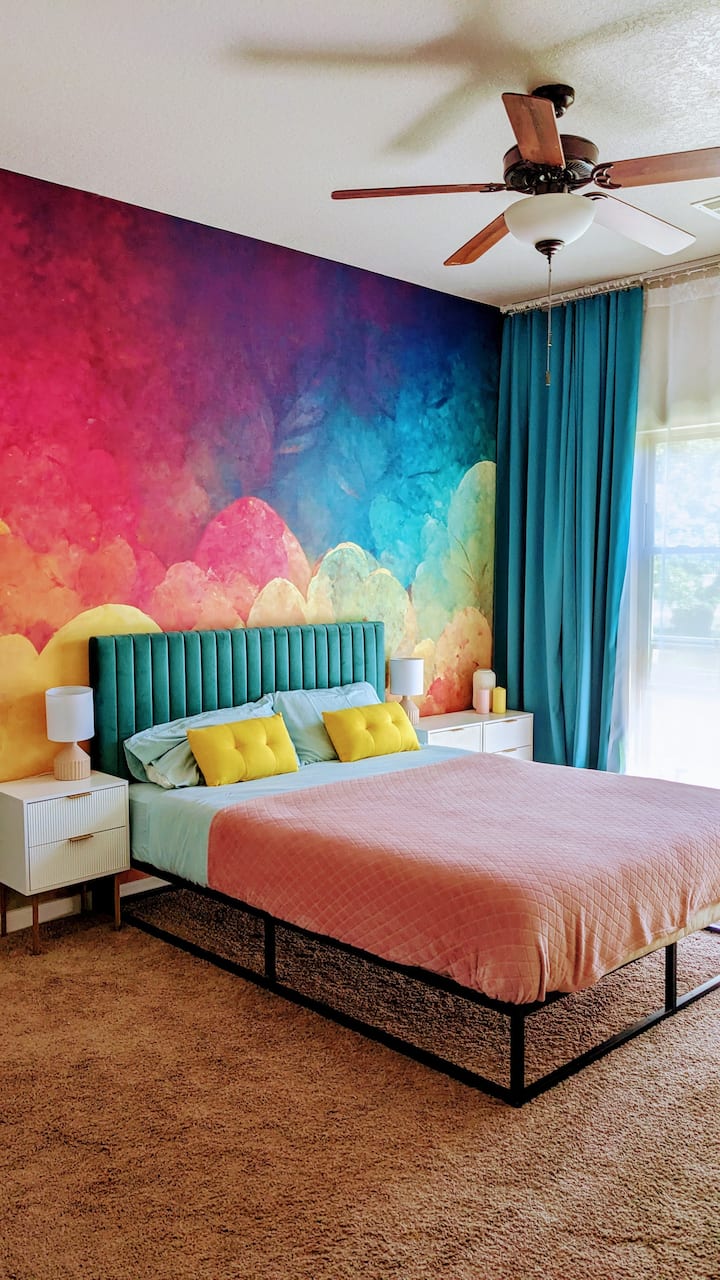 Krasna spavaća soba u duginim bojama s bračnim krevetom i dvosjedom.