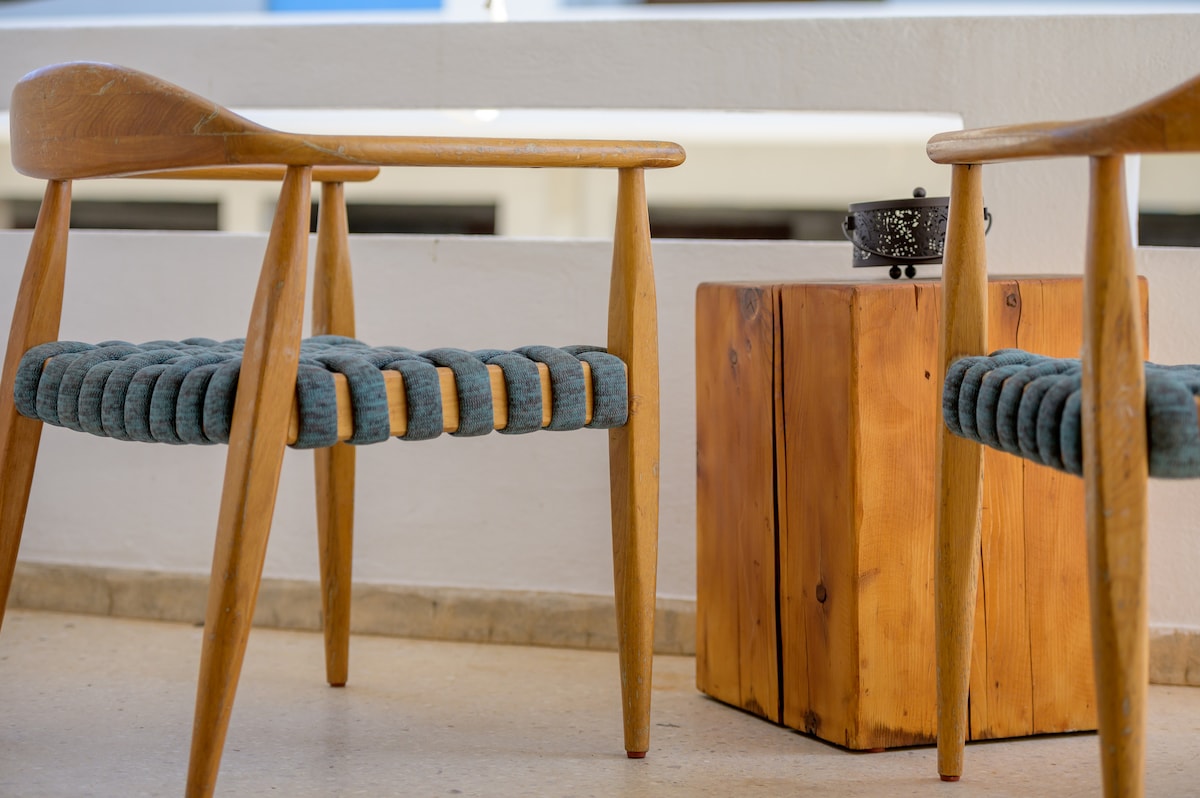Two wooden chairs featuring woven seat designs are positioned next to a rustic wooden side table. The neutral flooring provides a contrasting backdrop, while the overall arrangement creates a cozy corner suitable for relaxation.