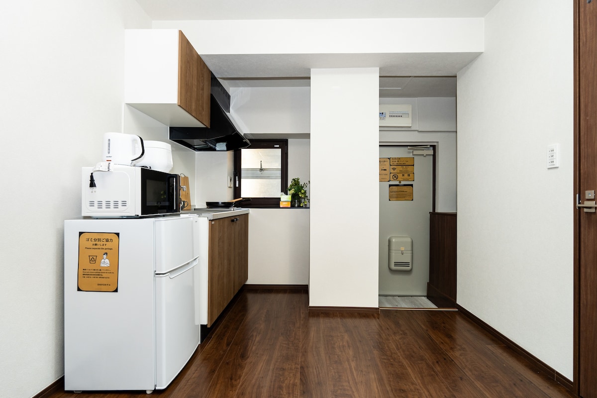 Compact kitchen with a white refrigerator, microwave, wooden cabinets, and dark wood flooring.