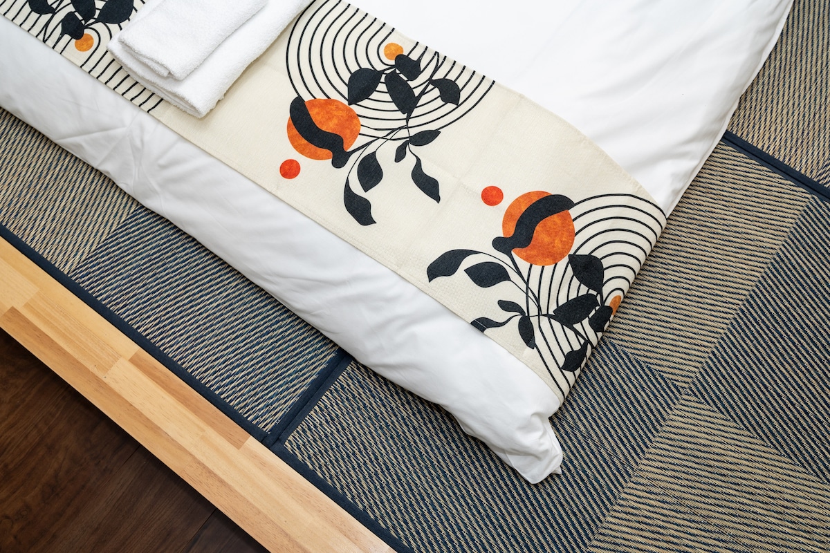 Bed with white sheets and a patterned runner on a traditional tatami mat floor.