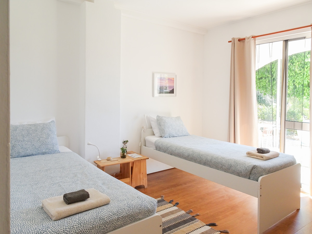 Ikiwa na vitanda viwili vya mtu mmoja, chumba hiki kina milango ya Kifaransa inayoelekea kwenye baraza ya kujitegemea ya nyumba iliyo na mandhari nzuri ya bustani. Mwangaza wa asili hufurika kwenye sehemu hiyo, na kuunda mazingira angavu na ya kukaribisha. Vitambaa vya kitanda na taulo vimetolewa. 