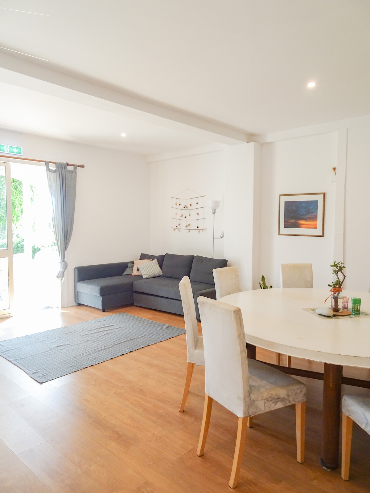 Chumba cha Kuishi chenye nafasi kubwa chenye mwanga wa asili kutoka milango ya Kifaransa inayoelekea kwenye baraza ya kujitegemea. Pumzika kwenye sofa ya kisasa yenye umbo la L huku ukifurahia Televisheni mahiri, au kukusanyika kwenye meza ya kulia ya mviringo. 

