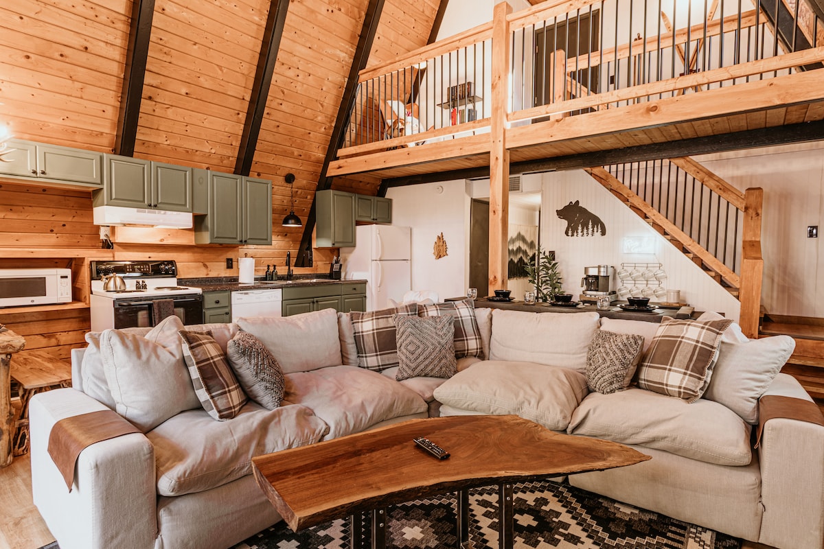 ¡Relájate en nuestro concepto abierto y cómoda sala de estar con una enorme chimenea original! Disfruta de las líneas de techo empinadas que se extienden hasta los pisos, formando la icónica forma de A que define este estilo clásico de cabaña. 